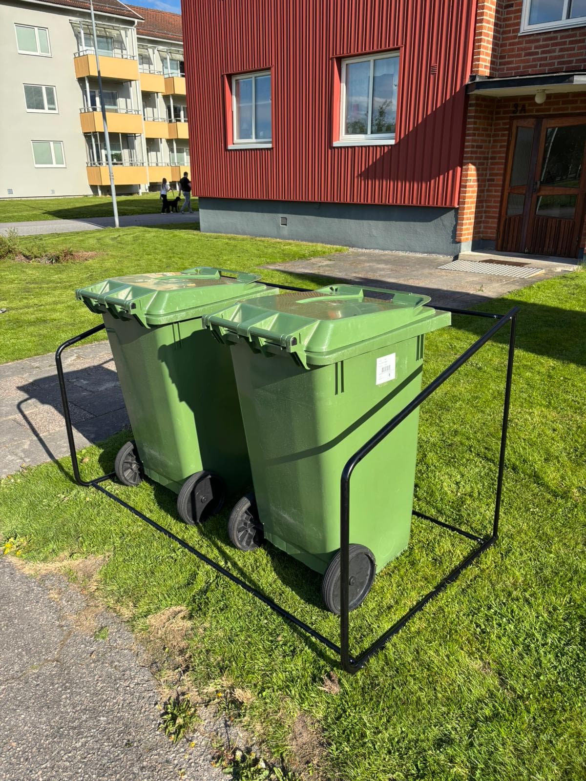 Semachs öppna soptunnegarage med två gröna soptunnor utanför ett flerbostadshus