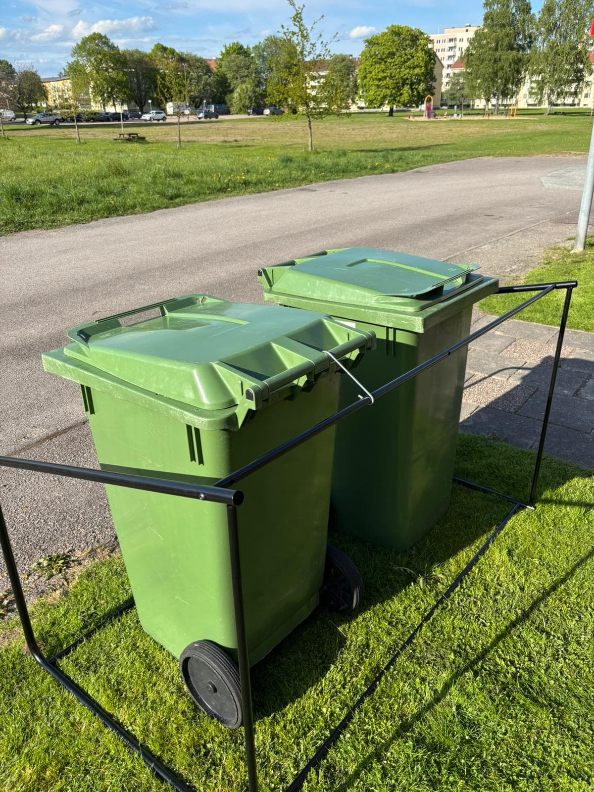 Semachs öppna soptunnegarage uppställt vid en park med flerbostadshus i bakgrunden
