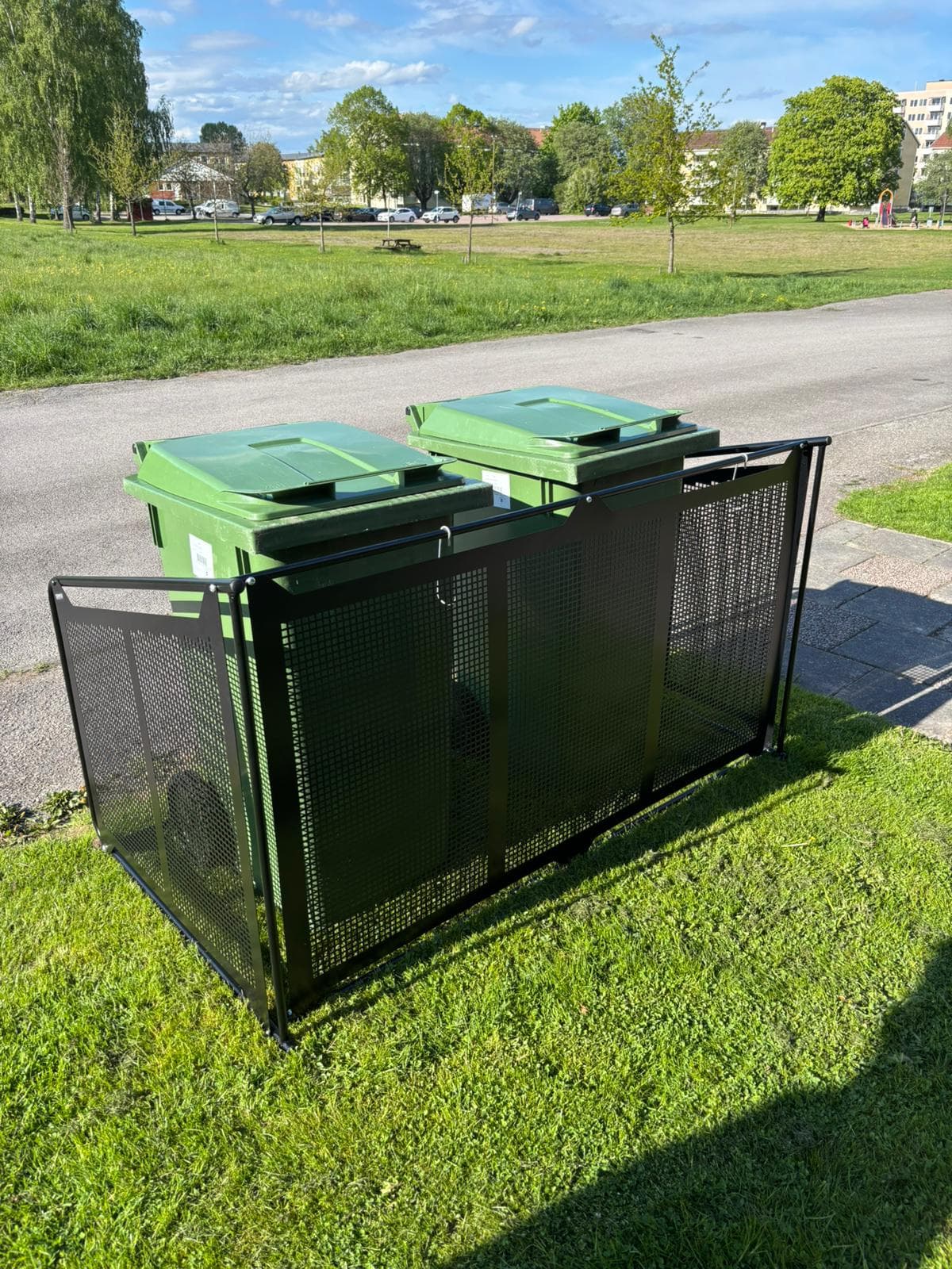 Semachs soptunnegarage med täcksidor sett snett framifrån vid en park, två gröna soptunnor inuti