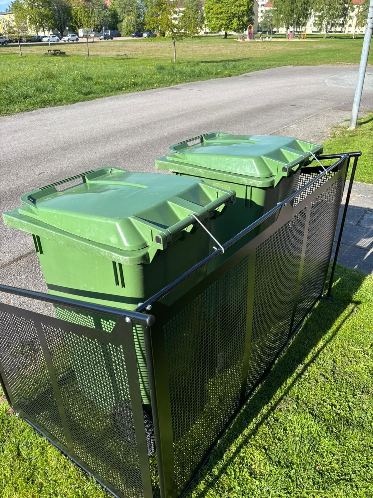 Semachs soptunnegarage med täcksidor sett från sidan vid en park, två gröna soptunnor inuti