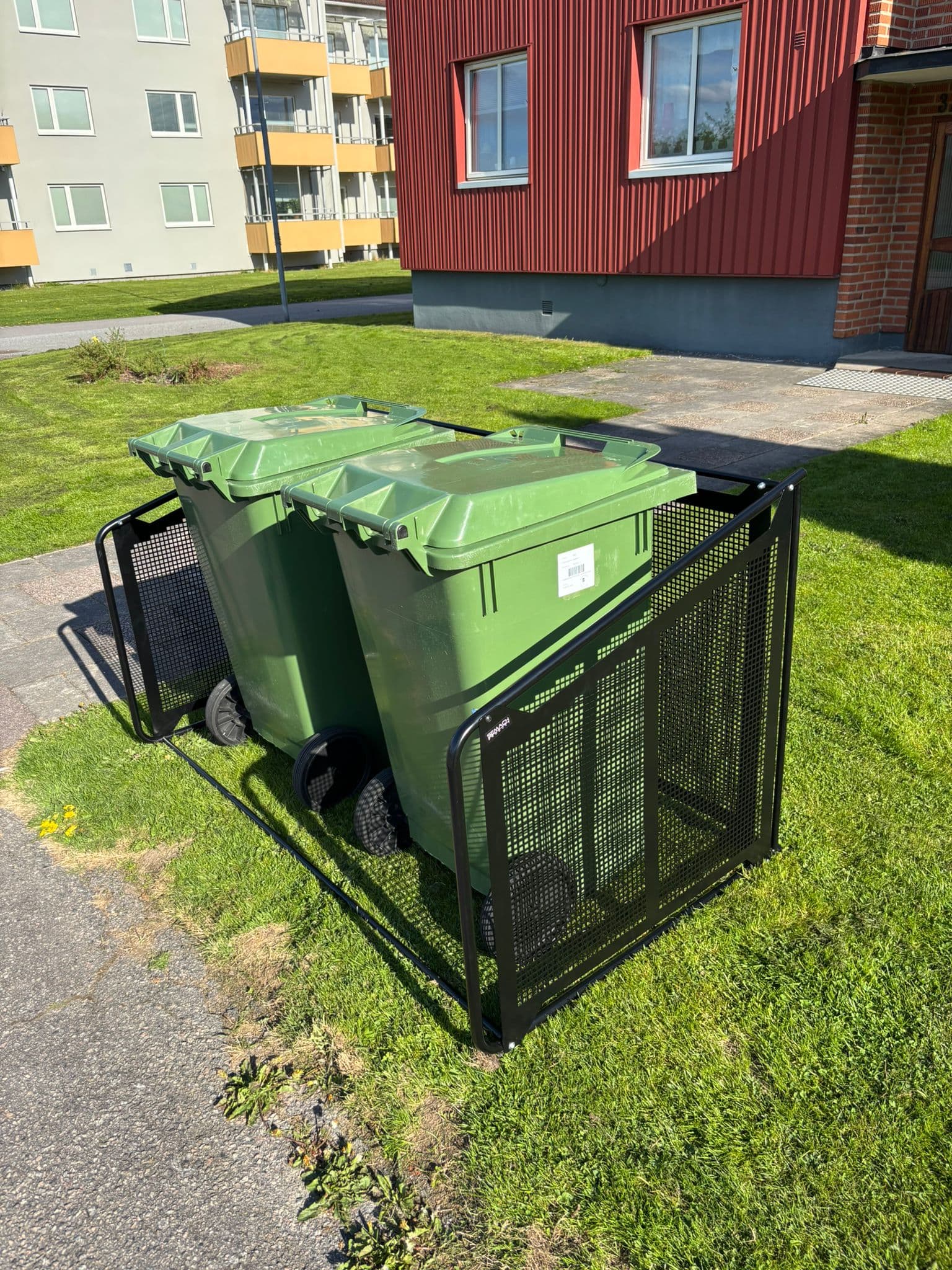 Semachs soptunnegarage med täcksidor och två gröna soptunnor utanför ett rött radhus