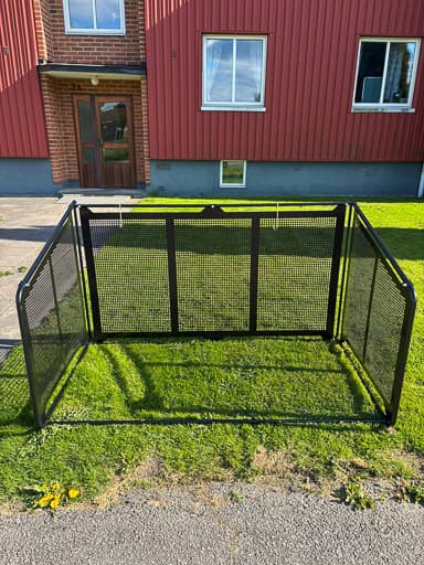 Tomt Semach soptunnegarage med täcksidor sett framifrån, uppställt på en gräsmatta utanför ett rött hus