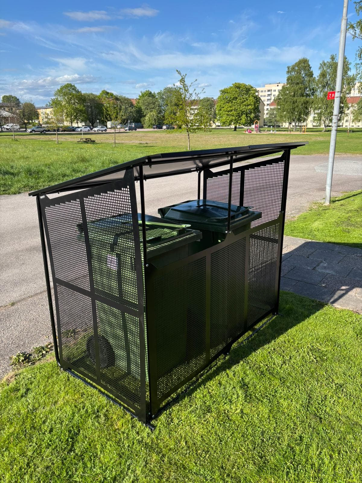 Semachs soptunnegarage med tak och täcksidor vid en parkering, med ett av tunnornas lock öppet