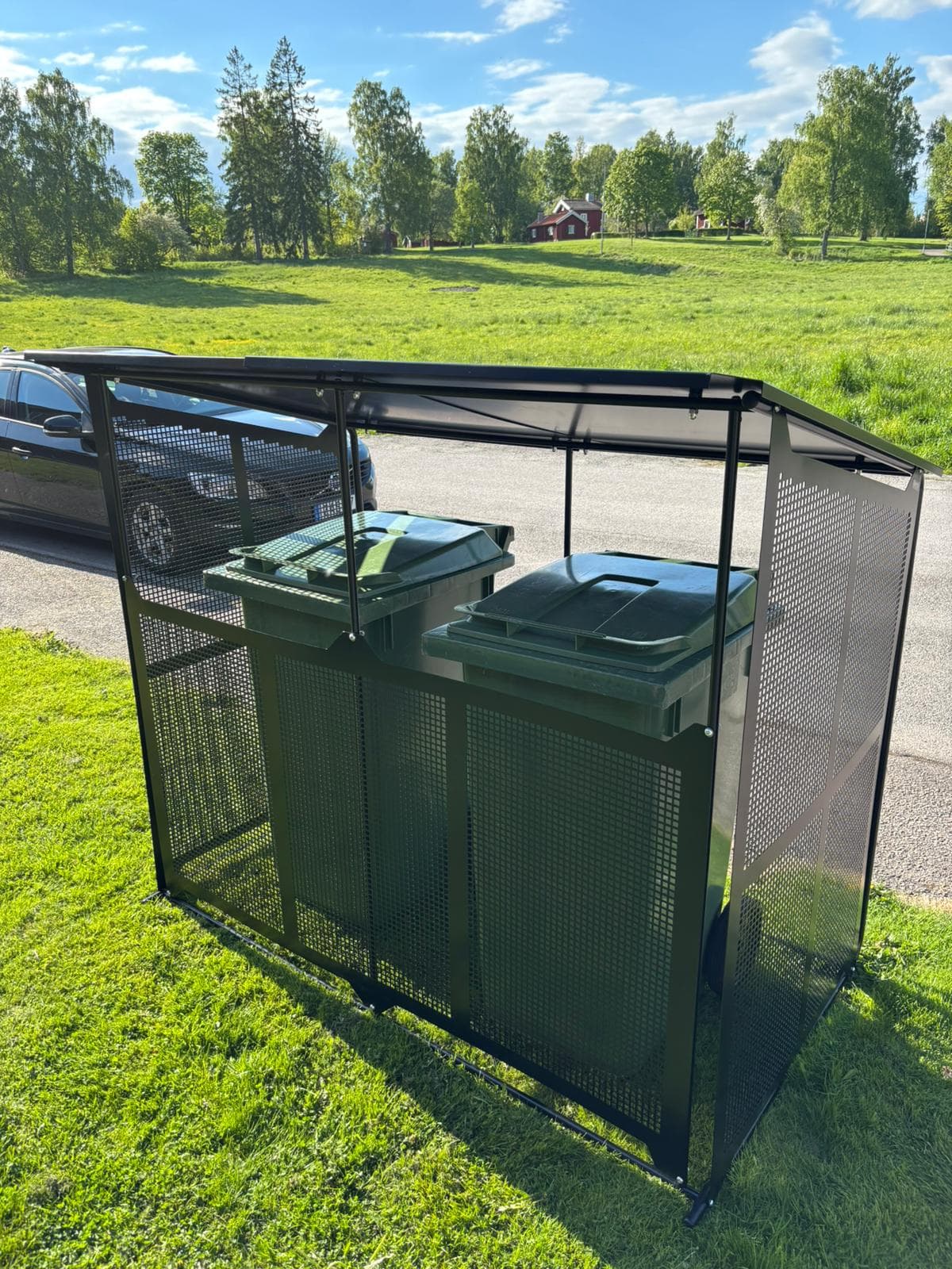 Semachs soptunnegarage med tak och täcksidor uppställt på gräsmattan vid en parkering med park i bakgrunden