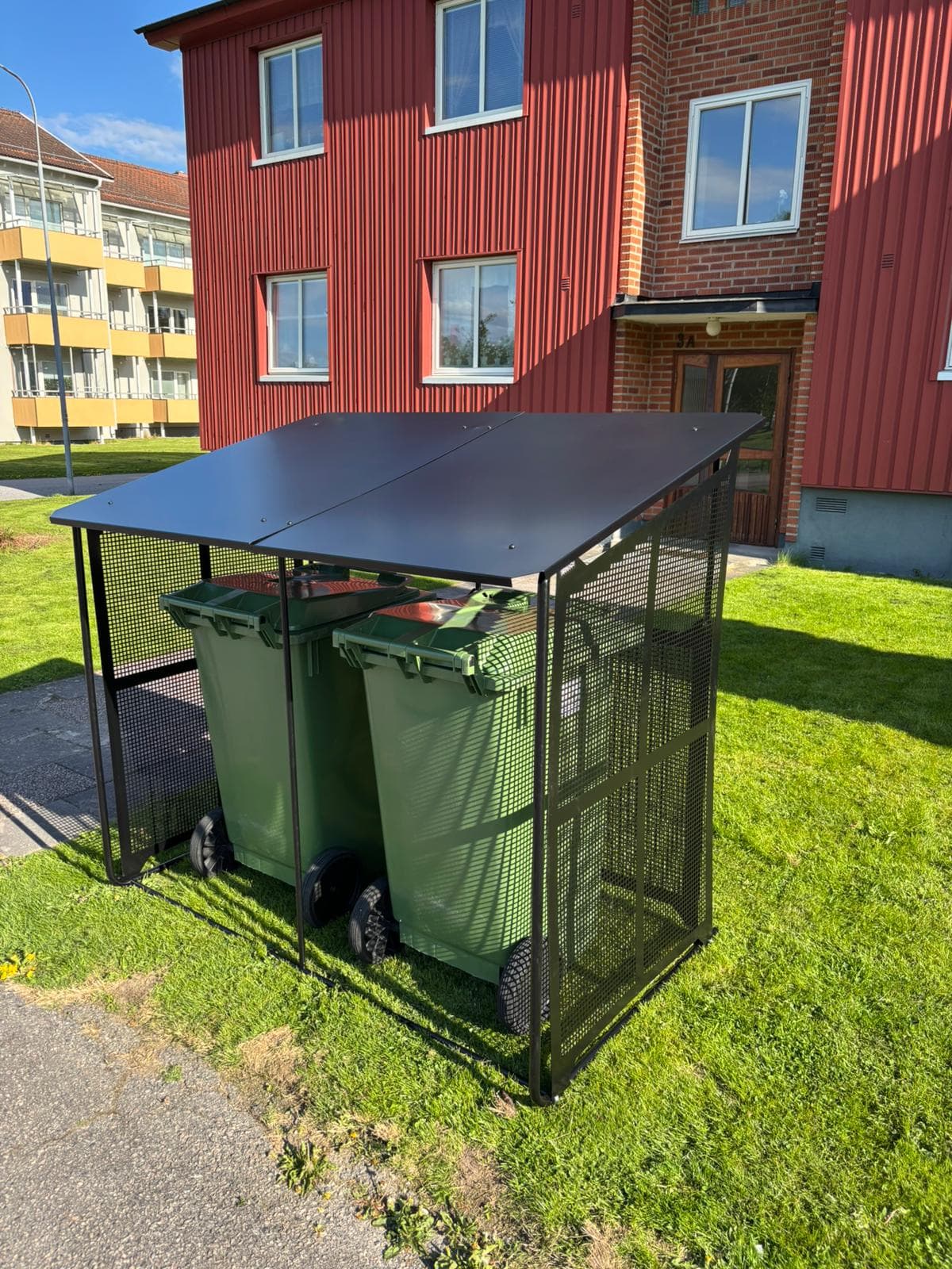 Semachs soptunnegarage med tak och täcksidor utanför ett rött radhus, med ett av tunnornas lock öppet